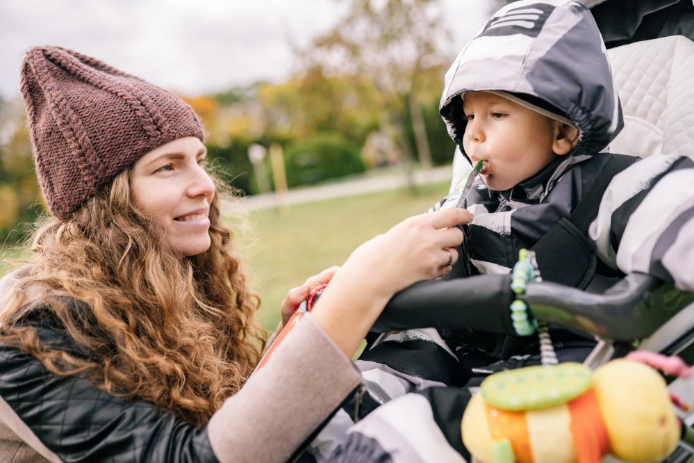 mum feeding infant food pouch in pushchair