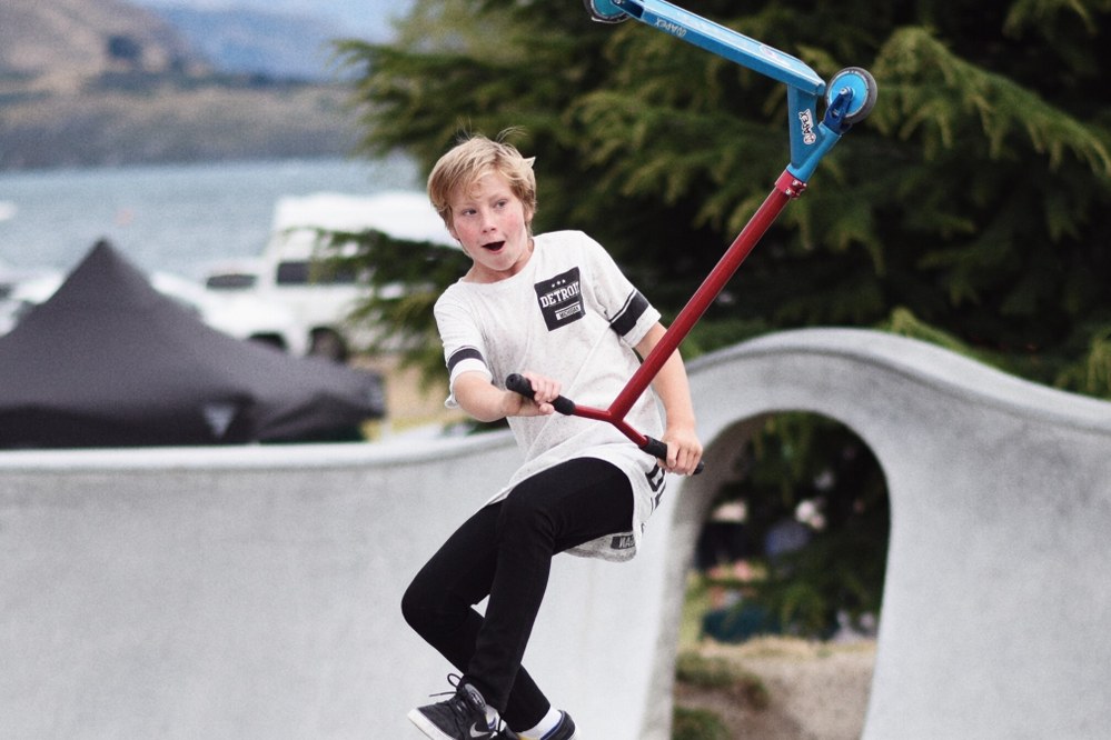 boy using stunt scooter in skateboard park